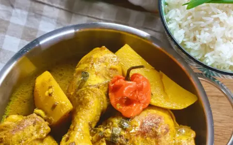 Colombo de poulet mit Kartoffeln und einer scharfen Chili, daneben eine Schüssel Reis.