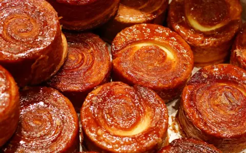 Nahaufnahme von karamellisierten Kouign Amann Gebäckstücken mit spiralförmiger Teigstruktur.