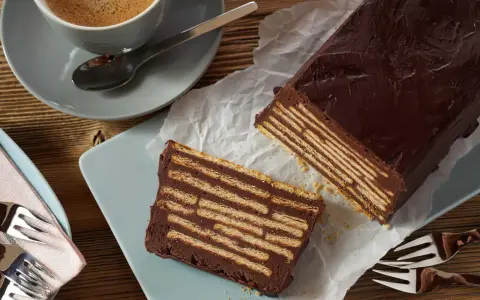 Ein Stück Schokoladenkuchen, der wie ein kalter Hund aussieht, mit Keksen und Schokoladencreme geschichtet. Daneben eine Tasse Kaffee.