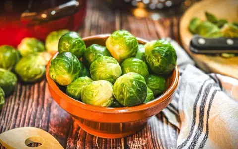 Frischer Rosenkohl in einer Schale, bereit, rosenkohl zuzubereiten wie Oma. Ein Holzlöffel liegt daneben.