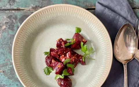 Ein köstlicher Rote Bete Feta Salat mit frischer Petersilie, serviert auf einem rustikalen Teller. Daneben liegen Löffel und Gabel.