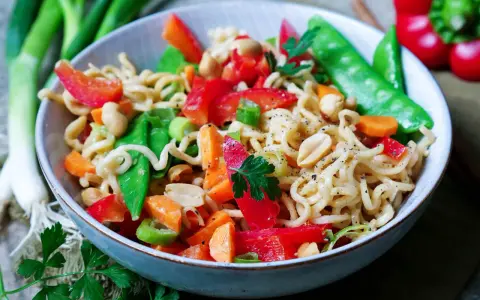 Bunter mie nudelsalat mit Erdnüssen, Paprika, Zuckerschoten und Karotten, garniert mit Petersilie.