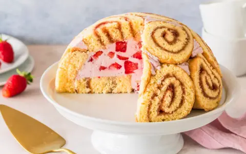 Halbierte Erdbeer Charlotte auf einer Tortenplatte, gefüllt mit Erdbeercreme und frischen Erdbeeren, umhüllt von Biskuitrollen.