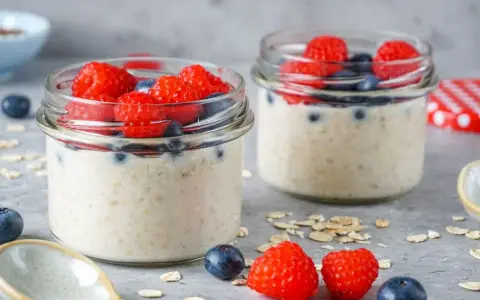 Zwei Gläser mit Overnight Oats, garniert mit frischen Himbeeren und Blaubeeren. Perfekt für ein leckeres, low carb Frühstück.
