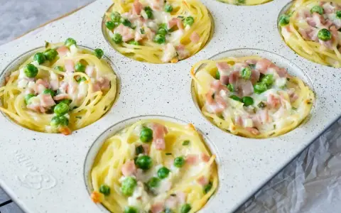 Köstliche Muffins aus nudeln vom vortag, gefüllt mit Erbsen und Schinken, überbacken mit Käse.
