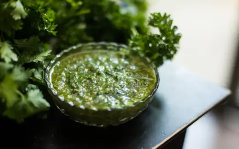 Frische Kräuter umgeben eine Schale mit leuchtend grünem Chimichurri. Was ist Chimichurri? Eine würzige argentinische Sauce aus Petersilie, Knoblauch und Essig.