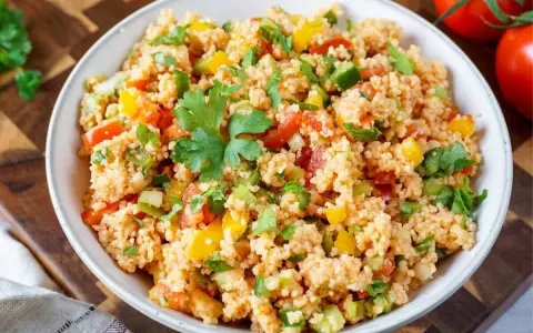 Frischer Couscous-Salat mit Tomaten, Paprika und Petersilie, garniert mit einem Petersilienblatt.
