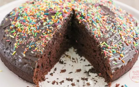 Schokoladenkuchen ohne Mehl und Ei, mit glänzender Glasur und bunten Streuseln. Ein Stück fehlt, was Lust auf mehr macht.