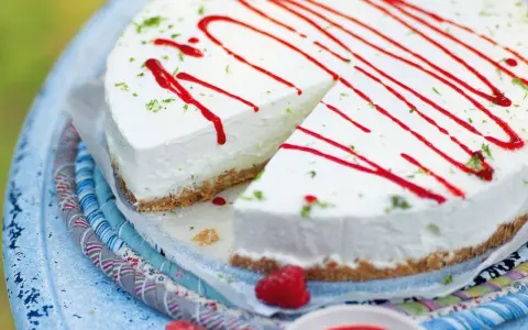 Cremiger Kuchen ohne Backen, dekoriert mit rotem Sirup und Limettenabrieb. Ein Stück ist bereits angeschnitten.
