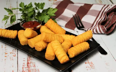Goldbraune Kroketten, frisch zubereitet, liegen auf einem schwarzen Teller. Dazu gibt es Ketchup und frische Petersilie. Perfekt zum selber machen!