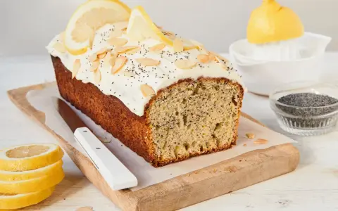 Saftiger zitronen mohn kuchen mit weißem Zuckerguss, Mandelsplittern und Mohn bestreut. Zitronenscheiben zieren die Oberseite.