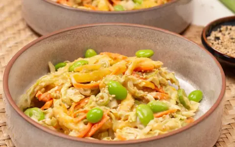Ein cremiger asiatischer Salat mit knackigem Kohl, Karottenstreifen und Edamame, garniert mit Sesam.