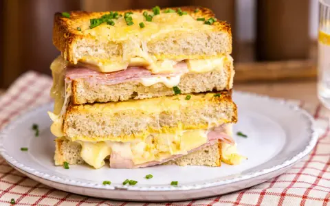 Ein gestapelter Croque Monsieur mit geschmolzenem Käse, Schinken und Schnittlauch auf einem Teller.