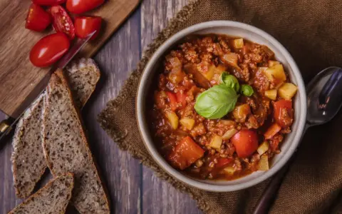 Herzhaftes Bauerntopf Rezept: Hackfleisch, Kartoffeln und Tomaten in einer Schüssel, garniert mit Basilikum. Dazu gibt es rustikales Brot.
