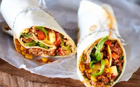 Zwei leckere wraps mit hackfleisch, Mais, Tomaten und Salat, serviert auf Backpapier.