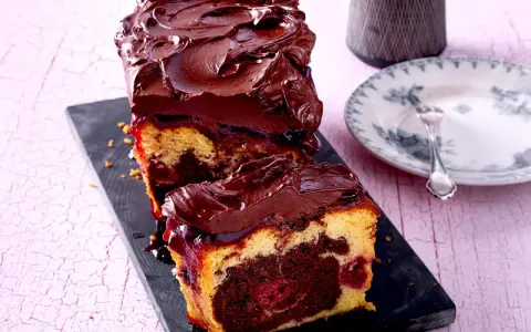 Saftiger Marmorkuchen mit Kirschen, überzogen mit dunkler Schokoladenglasur. Ein Stück ist bereits angeschnitten und zeigt die köstliche Marmorierung.