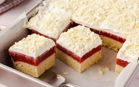 Schneeweiße Sahne und rote Fruchtschicht auf hellem Boden, bestreut mit weißer Schokolade. Ein köstlicher Frau Holle Kuchen, der zum Reinbeißen einlädt.
