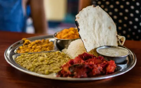 Vielfalt an indischen Gerichten auf einer Thali-Platte: Reis, Linsen, Curry und Papadum.
