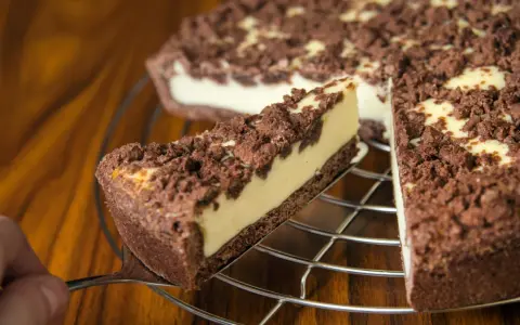 Ein Stück russischer Zupfkuchen wird aus dem Ganzen gehoben. Der Kuchen hat einen dunklen Boden, eine helle Füllung und eine krümelige Schokoladenstreusel-Decke.