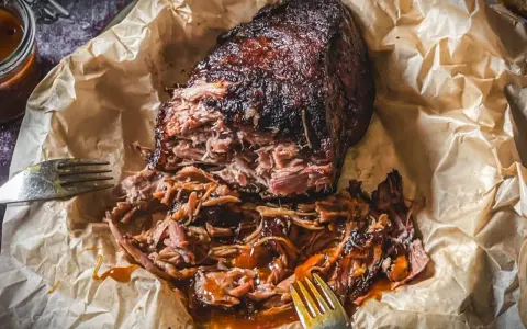 Saftiges pulled pork, zart zerfallen, mit BBQ-Sauce übergossen, auf Backpapier mit Gabeln.