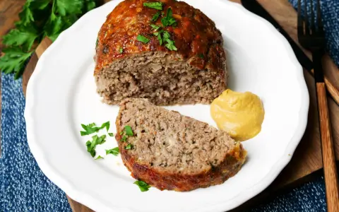 Saftiger hackbraten im ofen, auf einem Teller mit Senf und Petersilie garniert.