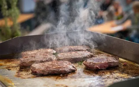 Mehrere saftige Steaks brutzeln auf einer heißen Platte. Dampf steigt auf und zeigt, wie man ein Steak richtig braten kann.