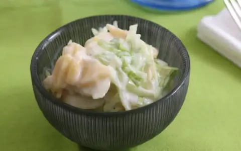 Ein cremiger Kartoffelsalat mit Joghurt und knackigem Gemüse, serviert in einer dunklen Schüssel auf einem hellgrünen Tischtuch.