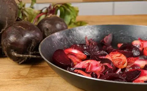 Rote Bete wird in einer Pfanne zubereitet, ein köstliches Hauptgericht. Frische Rote Bete liegt daneben.
