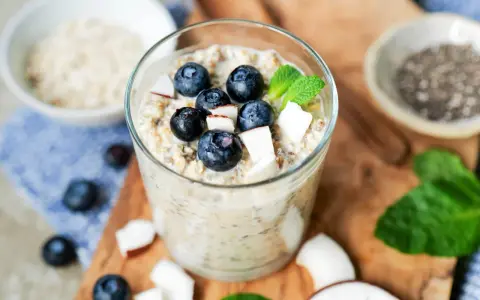 Ein Glas cremiger Overnight Oats mit Blaubeeren, Kokosnuss und Minze. Perfekt für ein schnelles Frühstück.