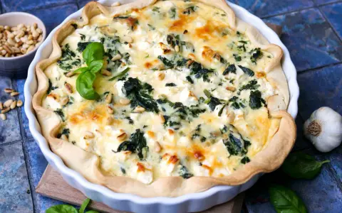 Herzhafte Quiche mit Spinat und Feta, garniert mit Pinienkernen und Basilikum.