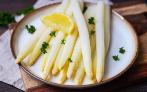 Frischer weißer Spargel, perfekt gekocht, garniert mit Petersilie und einer Zitronenspalte auf einem Teller. Ein Genuss, wenn Spargel Saison hat.