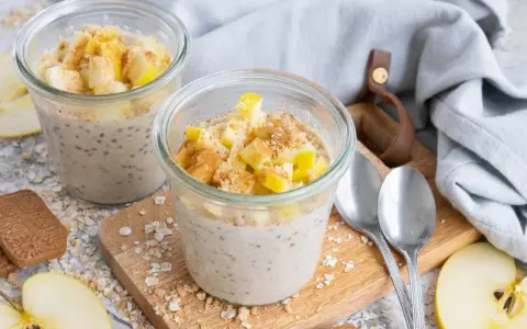 Zwei Gläser mit Overnight Oats Grundrezept, garniert mit Apfelstücken und Zimt. Perfekt für ein schnelles Frühstück.