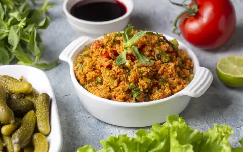 Ein köstliches Kisir-Rezept mit Bulgur, Tomaten und Kräutern, garniert mit Minze. Daneben Cornichons, Granatapfelsirup, Limette und ein frischer Kopfsalat.