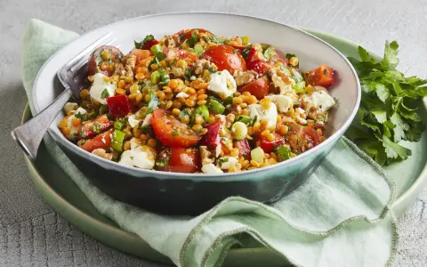Ein bunter, gesunder rote Linsen Salat mit Tomaten, Feta und Nüssen, appetitlich in einer Schüssel serviert.