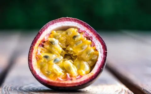 Eine aufgeschnittene Passionsfrucht mit saftigem, gelbem Fruchtfleisch und schwarzen Kernen liegt auf Holzplanken. Ein Genuss, diese Passionsfrucht zu essen!