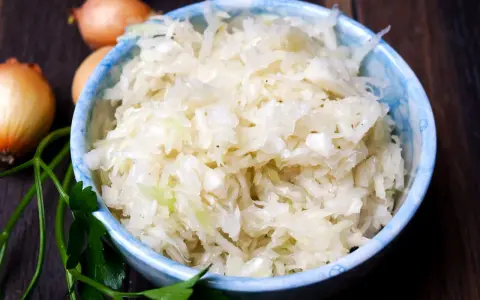 Schüssel mit frisch zubereitetem Krautsalat, daneben Zwiebeln und Petersilie. Perfekt, um Krautsalat selbst zu machen!