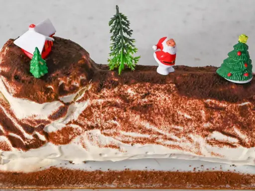 Eine festliche bûche de noël deutsch, verziert mit Weihnachtsmann, Bäumen und einem Haus.