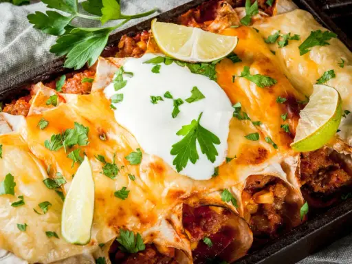 Herzhafte Enchiladas mit geschmolzenem Käse, saurer Sahne und Limettenspalten. Ein köstliches Enchiladas Rezept, das man probieren muss!