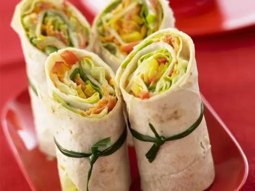 Vier gesunde wraps gefüllt mit knackigem Salat, Paprika und Karotten, kunstvoll mit grünen Bändern zusammengebunden.