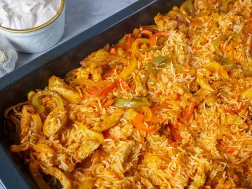 Herzhaftes One Pot Reis Ofen Gericht mit Hähnchenstreifen und bunten Paprikastreifen, serviert in einer schwarzen Auflaufform.