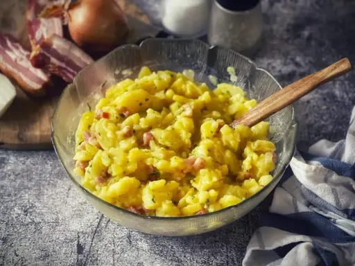 Schüssel mit warmem Kartoffelsalat, garniert mit Speck und Zwiebeln, bereit zum Servieren.