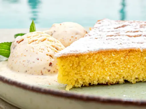 Ein Stück mallorquinischer Mandelkuchen mit zwei Kugeln Eis und Minze, serviert auf einem Teller am Pool.