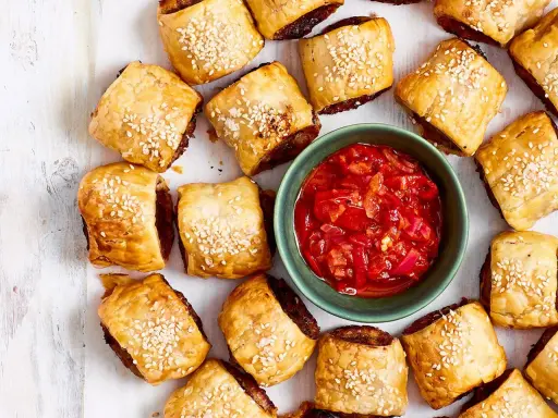 Goldbraune Würstchenschnecken mit Sesam, daneben eine Schale mit roter Chutney-Sauce. Perfekt, um schnelles Fingerfood am Vortag zuzubereiten.