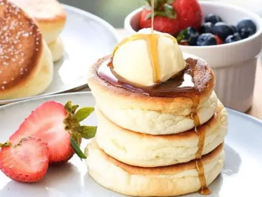 Fluffige japanische Pancakes mit einer Kugel Eis, Sirup und frischen Beeren.