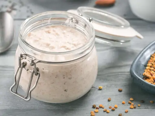 Ein Glas cremiger Haferflocken-Pudding steht bereit, daneben eine Schale mit Pollen und ein Löffel.