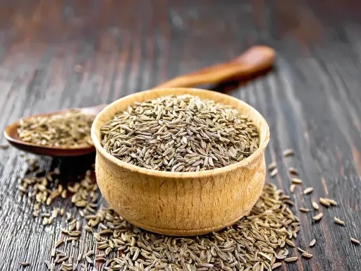 Ein Holzlöffel und eine Schale sind gefüllt mit Kümmelsamen. Was ist Kümmel? Ein beliebtes Gewürz für Brot und deftige Gerichte.