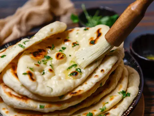 Frisch gebackenes Naan Brot wird mit Butter bestrichen und mit Kräutern bestreut.