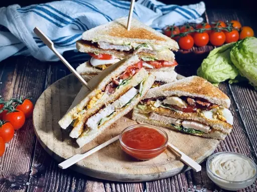 Ein gestapelter Club Sandwich mit Hühnchen, Speck, Ei und Tomaten, serviert mit Ketchup und Mayonnaise.