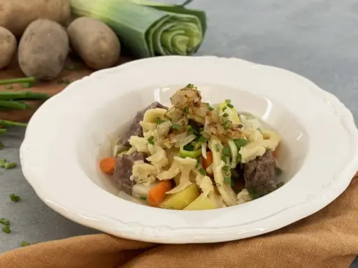 Herzhafter Gaisburger Marsch mit zarten Spätzle, Rindfleisch, Kartoffeln und Karotten, garniert mit Röstzwiebeln und Schnittlauch.