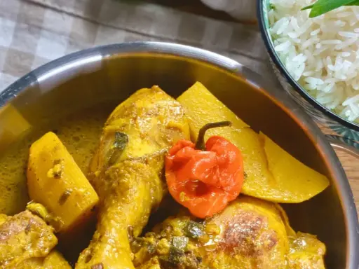 Colombo de poulet mit Kartoffeln und einer scharfen Chili, daneben eine Schüssel Reis.